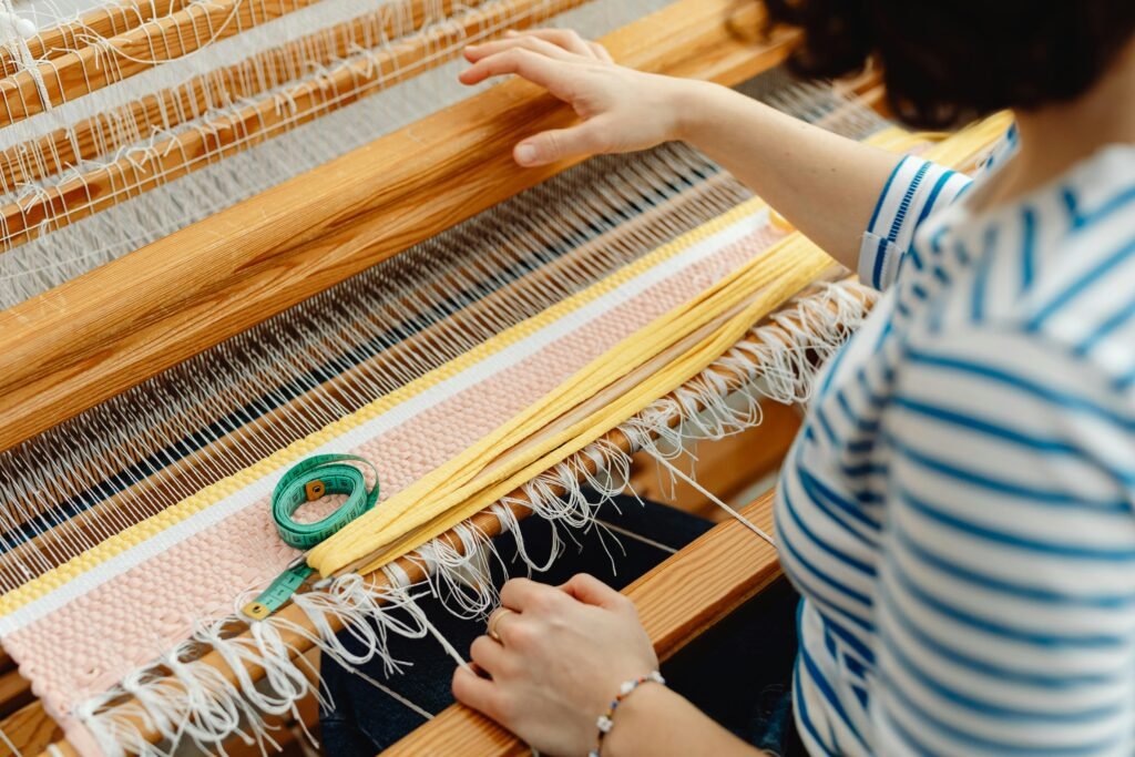 Close-up of an artisan's hands weaving on a wooden loom, showcasing textile craftsmanship.