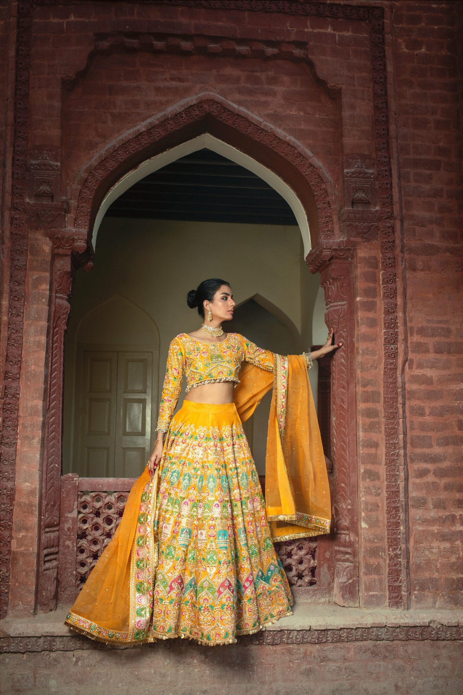 Indian bride posing gracefully in a colorful lehenga against a vintage architectural backdrop.