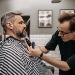 A professional barber precisely trimming a client's beard in a modern barbershop.